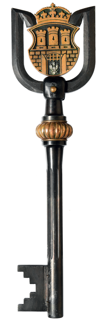 (336) Nowy klucz symbolizujący władzę nad Krakowem, wykonany w Instytucie Odlewnictwa w Krakowie, używany od roku 2000. Wielkość podobna
do klucza „ratuszowego” – długość 31,5 cm, szerokość w uchwycie 8,5 cm, w tymże uchwycie duży herb miasta. Ta ekspozycja herbu powoduje, że klucz
ten nazywamy tutaj kluczem „herbowym”. Jego powstanie wyprzedziło prace nad regulacją dotyczącą symboliki Krakowa, które Rada Miasta Krakowa
sfinalizowała w roku 2002. Stąd też rysunek herbu na kluczu nie uwzględnia jeszcze korekt niewiele później wprowadzonych
do obowiązującego kształtu herbu miasta (z zasobów UMK)