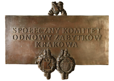 (283) Dawna tablica informacyjna z siedziby Społecznego Komitetu Odnowy Zabytków Krakowa – tu widoczny znak organizacji na motywie
królewskiego monogramu „K” (ze zbiorów SKOZK)