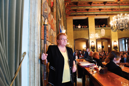 (392) Radna seniorka Rady Miasta VIII kadencji Teodozja Maliszewska 21 listopada 2018 r. trzykrotnym uderzeniem laski w prezydialny podest otwiera
pierwsze posiedzenie Rady tejże kadencji – zgodnie z tradycją sięgającą czasów staropolskich najstarszy wiekiem radny ma pewne prerogatywy, w tym
przypadku dotyczące otwarcia i poprowadzenia obrad do wyboru przewodniczącego Rady nowej kadencji (z zasobów UMK)