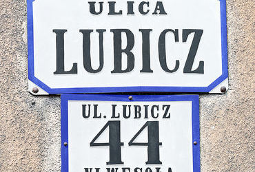 Fot. 29. W roku 1881 Rada Miasta Krakowa, utrzymując dotychczasowy podział na 8 dzielnic katastralnych (jedynie Dzielnicę I w miejsce nazwy „Kraków” nazwano „Śródmieściem”), wprowadziła nowe zasady ponumerowania orientacyjnego domów w mieście. Zasady te przetrwały do dzisiaj: numeracja domów ulicami (a nie dzielnicami katastralnymi, jak poprzednio), początek numerowania od strony bliższej Rynkowi Głównemu (na Stradomiu bliższej ul. Stradomskiej, na Kazimierzu bliższej ul. Krakowskiej), numery nieparzyste po prawej stronie. Wprowadzono jednolite dla całego miasta kolory tabliczek z nazwami ulic i tabliczek orientacyjnych z numerami domów: litery i cyfry koloru czarnego, tło białe, obwódki tablic niebieskie (DzRMK 1881, nr 1, s. 2–3). Przydzielone wówczas nowe numery domów pozostały już z reguły niezmienione do naszych czasów (zmiany w przynależności dzielnicowej ulic nie miały znaczenia dla numeru domu), natomiast sam wzór tabliczek wprawdzie był aktualny jeszcze w okresie okupacji, jednak już w okresie międzywojennym podlegał wymianie na znany nam co do kolorystyki z codzienności wzór nowy, z białymi literami i cyframi na niebieskim tle, z białą obwódką. Powyżej: 3) zaprezentowane obok tabliczki z domu przy ul. Lubicz (dziś postarzałe i pociemniałe) zgodnie z wytycznymi z roku 1881 pierwotnie wyglądały inaczej – na zdjęciu zrekonstruowano ówczesną kolorystykę.